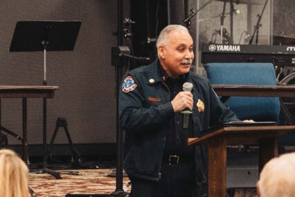 San Jose's fire chief speaks to a crowd indoors holding a microphone