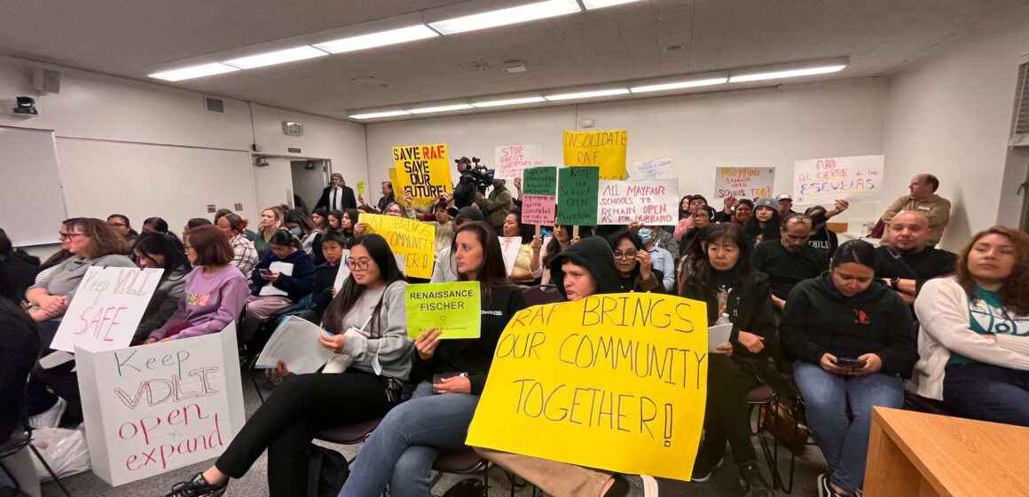 People sitting and holding signs at a school board meeting.