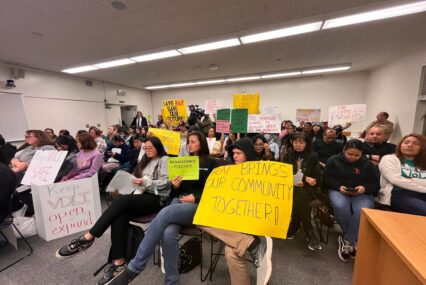 People sitting and holding signs at a school board meeting.