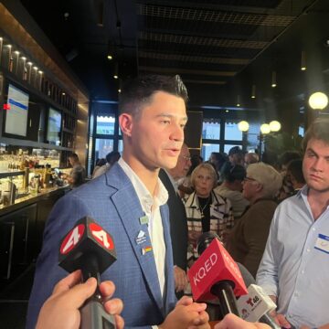 A man in a suit speaking into microphones inside a bar