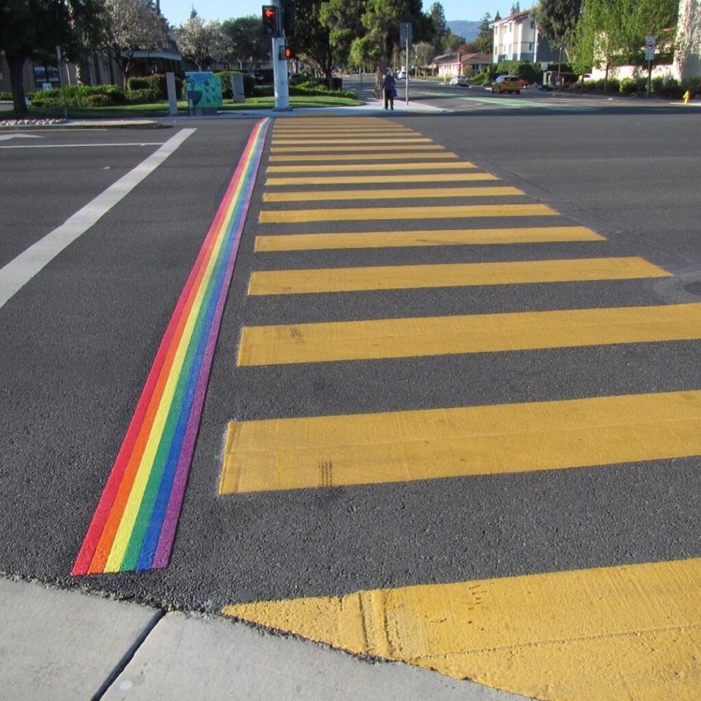 Photo of a crosswalk with a foot wide strip of rainbow to one side