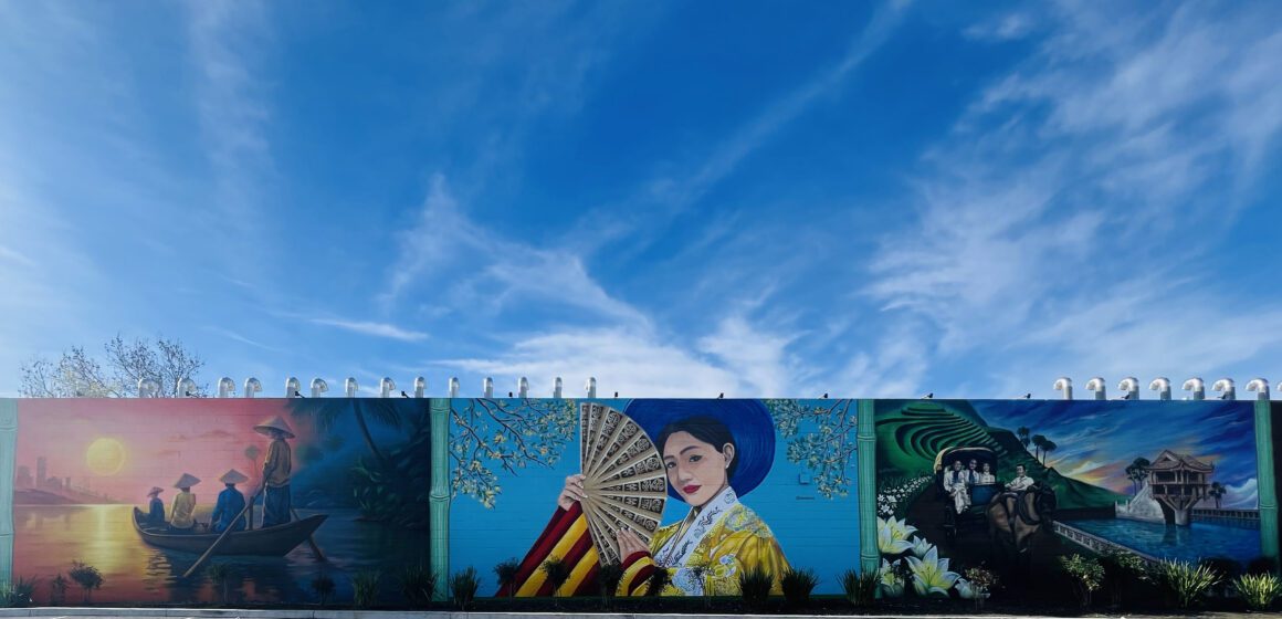 A three-panel mural with Vietnamese motifs on a wall with blue sky overhead