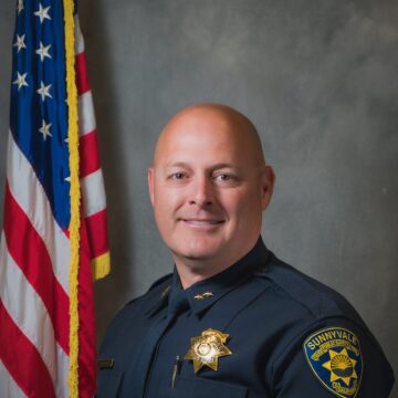 A public safety officer posing for a photo in front of an American flag