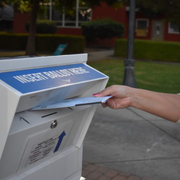 A hand putting a mail-in ballot in a secure drop box