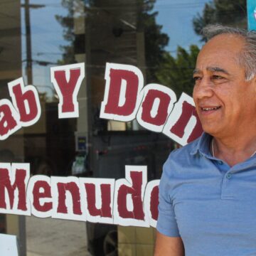 Un hombre parado frente a una tienda sonriendo y mirando fuera de cámara.