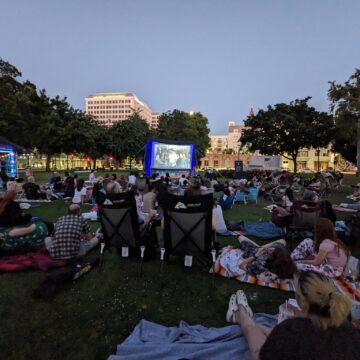 A crowd of people on a lawn watching an outdoor movie screening