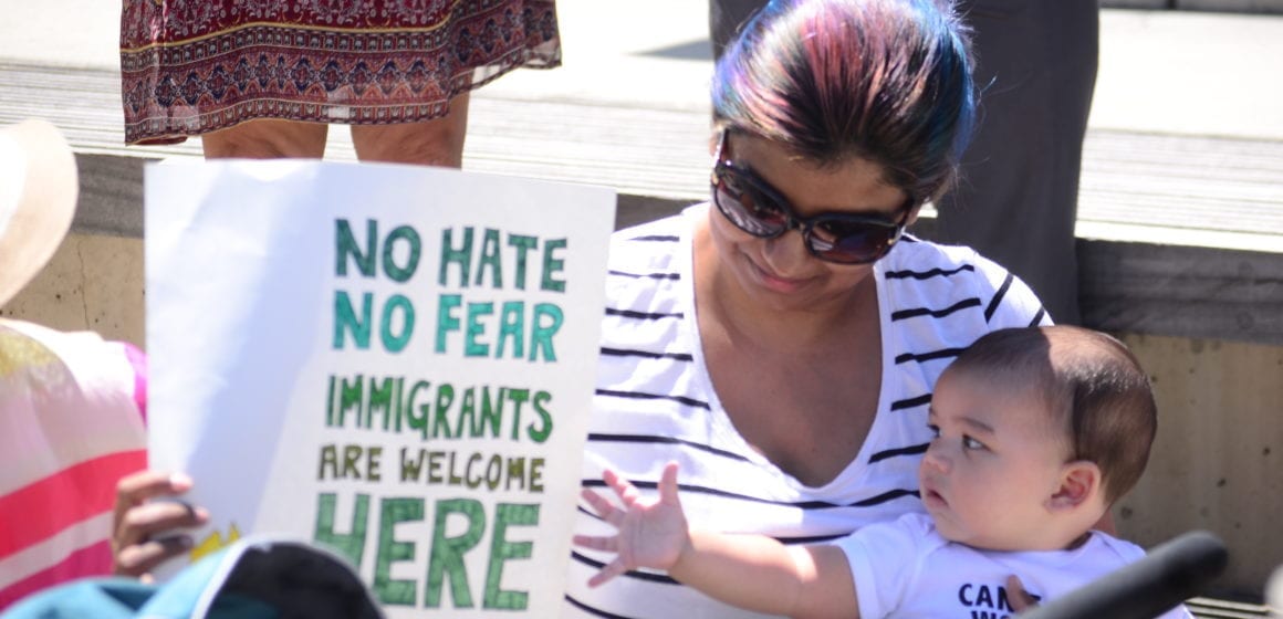 A woman sits holding a baby and a protest sign