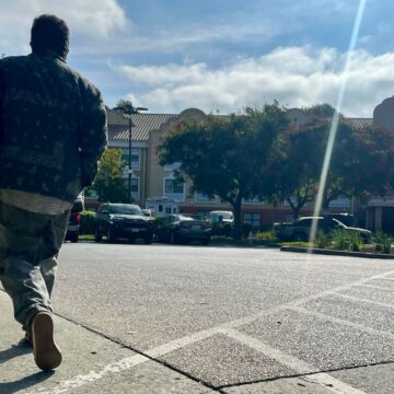 Un hombre caminando por la acera frente a un edificio de apartamentos.