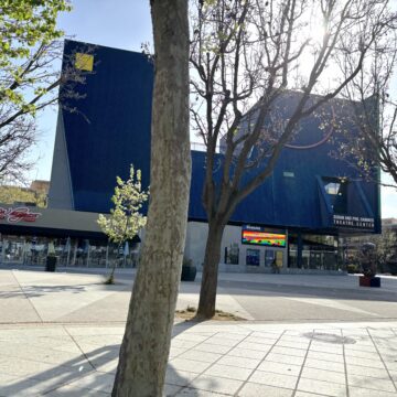 The blue building known as Hammer Theatre is in full view surrounded by trees as the sun rises in the background.