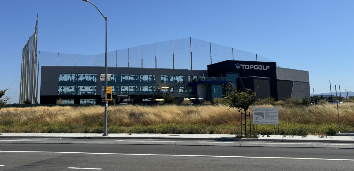 An across-the-street view of North San Jose's Topgolf location among dead grass and leaves.