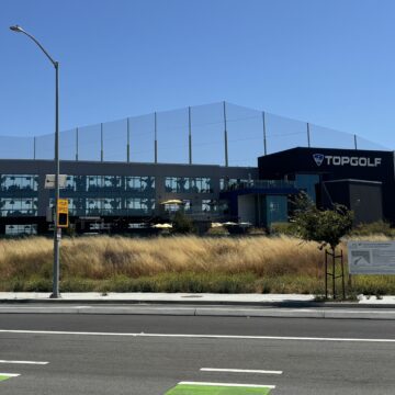 Una vista al otro lado de la calle de la sucursal de Topgolf en el norte de San José, entre césped muerto y hojas.