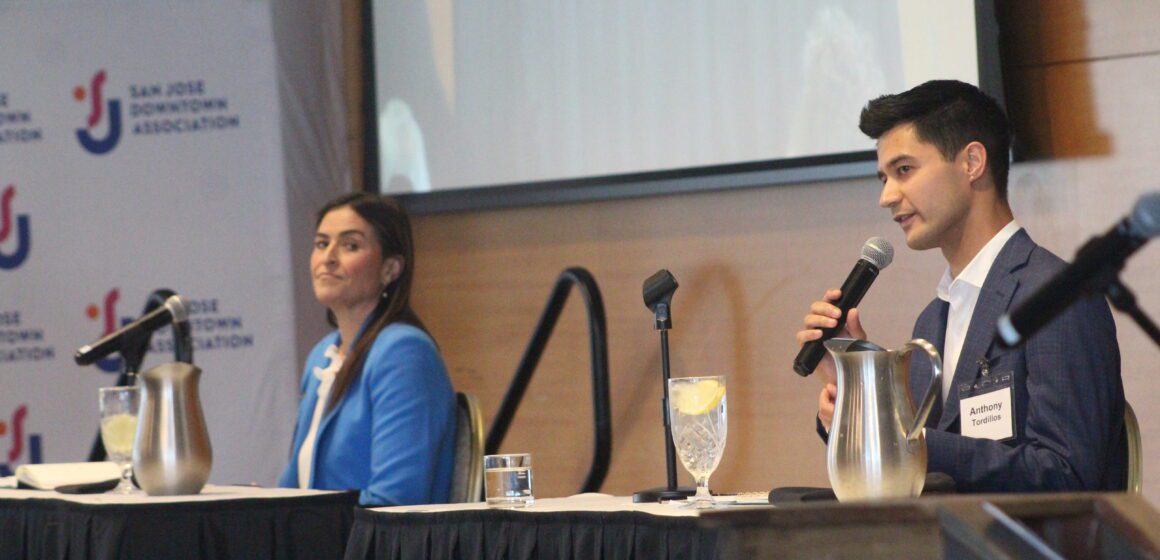Two people sitting at a dais in front of microphones take turns speaking.
