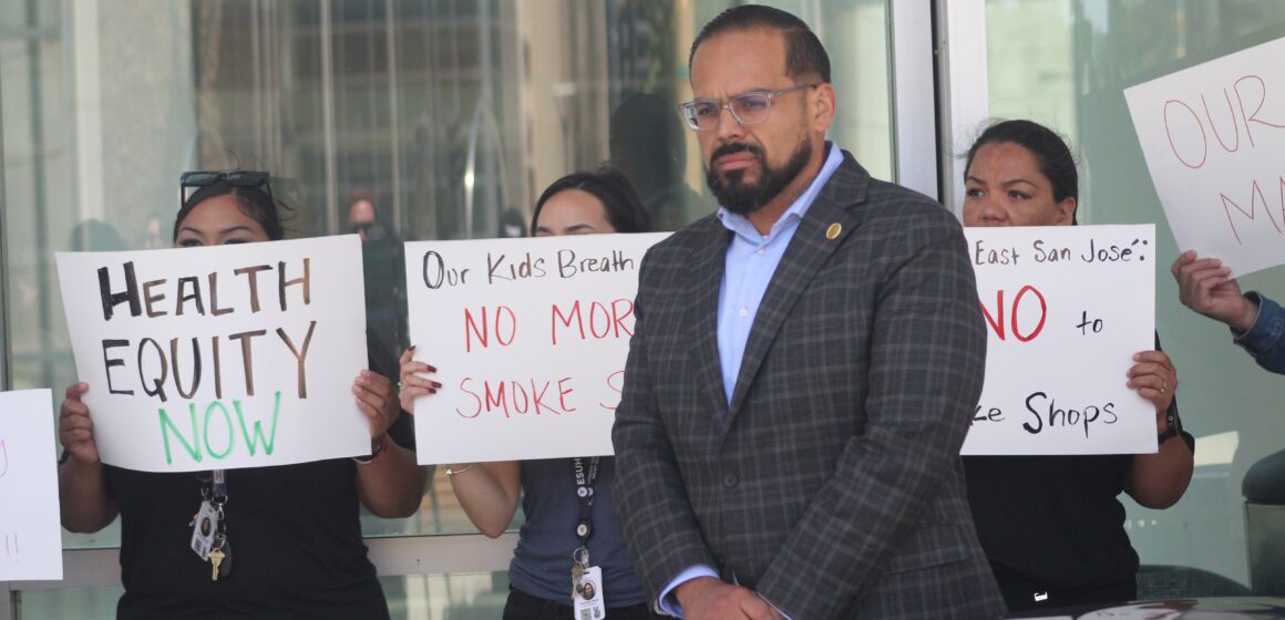 A man with glasses standing in front of a bunch of anti-smoking signs at San Jose City Hall.