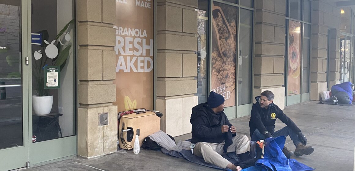 Two people sitting on the sidewalk in downtown San Jose