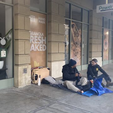 Dos personas sentadas en la acera en el centro de San José.