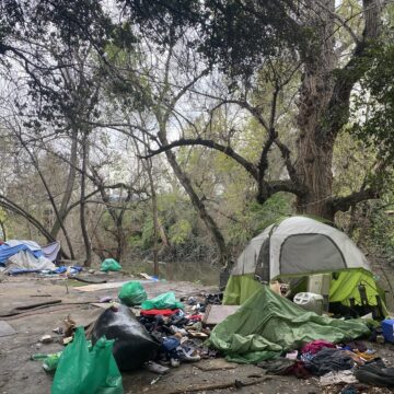 A homeless person's tent and belongings next to a creek
