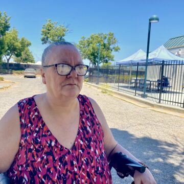 Una mujer con gafas se sienta afuera a la sombra.