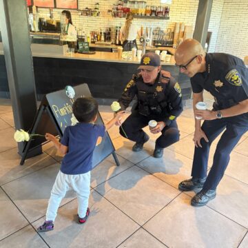 Phan Ngo, a bald tan Asian man wearing glasses and a Public Safety Officer uniform, squatting beside a tan child holding two yellow roses.