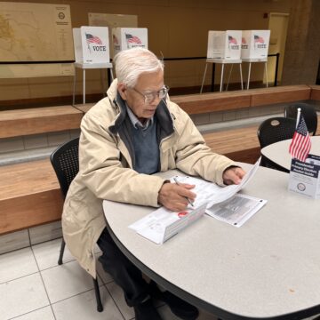 A man sits at a table and fills out his election ballot.