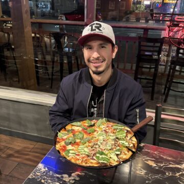 Một người đàn ông đang ngồi bên trong một chiếc bàn với một chiếc bánh pizza trước mặt