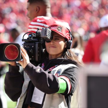 Una mujer sostiene una cámara de vídeo profesional en un partido de fútbol.