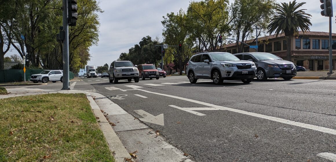 Un carril bici pintado al costado de una carretera asfaltada por el que pasan coches.