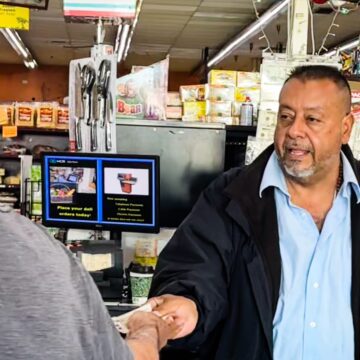 El dueño de un negocio en la caja registradora le está devolviendo dinero en efectivo a un cliente.