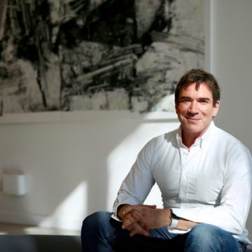 A man in a dress shirt sits looking at the camera