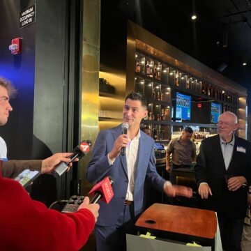 A man in a suit speaking into microphones inside a bar