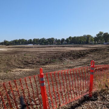 A vast, empty dirt lot with orange construction bollards at the entrance.