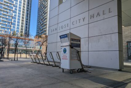 Một thùng phiếu trước bức tường có biển hiệu ghi dòng chữ "Tòa thị chính San Jose"